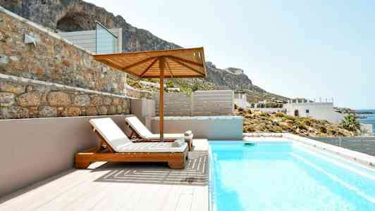 To solsenger under en parasoll ved et basseng med utsikt mot kysten og fjell. (AI-generert tekst)