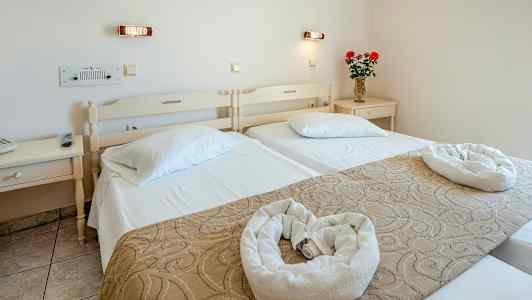 Et hotellrom med to enkeltsenger, pyntegjenstander og en vase med blomster på et nattbord. (AI-generert tekst)