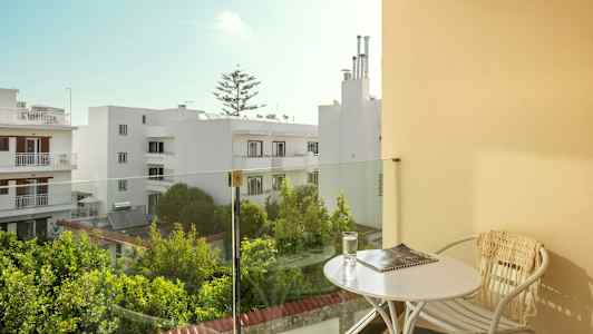 Balkong med bord og stol, utsikt over hvite bygninger og grøntområder. (AI-generert tekst)