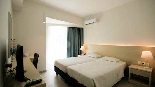 Hotellrom med to enkeltsenger, skrivebord med TV og lampe på nattbordet. (AI-generert tekst)