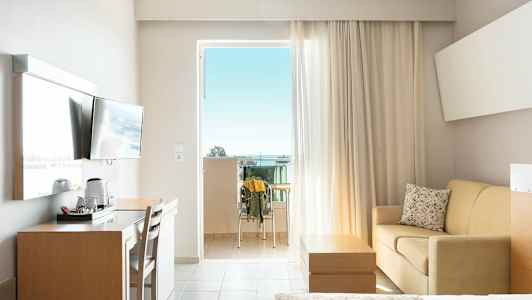 Hotellrom med balkong, TV, skrivebord, sofa og seng. (AI-generert tekst)