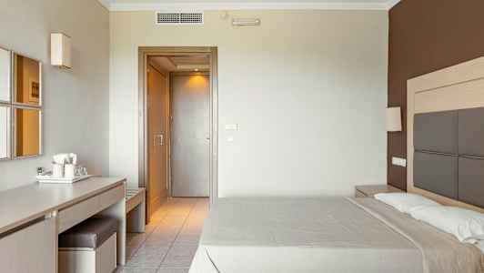 Hotellrom med en dobbeltseng, et skrivebord med stol og speil, samt en dør til øvrige rom. (AI-generert tekst)