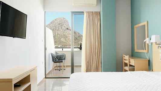 Hotellrom med en seng, skrivebord og balkong med utsikt over et fjell. (AI-generert tekst)