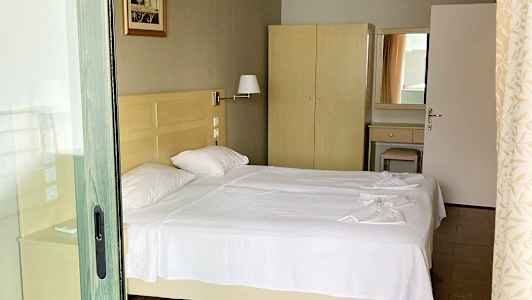 Bilde av et hotellrom med to enkeltsenger med hvitt sengetøy, et skap og et speil. (AI-generert tekst)