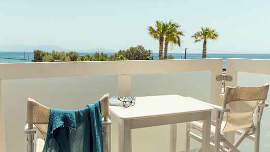 Utsikt fra en balkong med bord og stoler samt havutsikt i bakgrunnen. (AI-generert tekst)