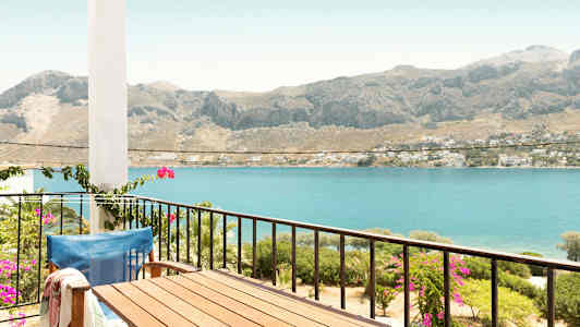 En balkong med bord og stol med utsikt over havet og fjell i bakgrunnen. (AI-generert tekst)