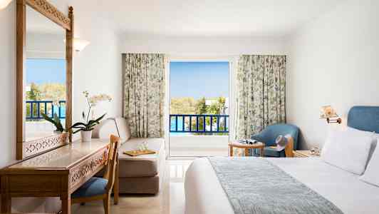 Et hotellrom med balkong, møbler inkludert seng, skrivebord, stol og lenestol. (AI-generert tekst)