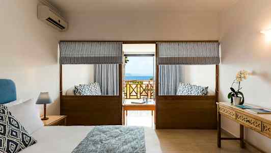 Et hotellrom med en dobbeltseng, sidebord og havutsikt fra en balkong. (AI-generert tekst)