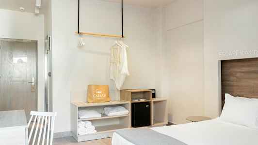 Et hotellrom med en oppredd seng, et garderobeområde og et bord med en stol. (AI-generert tekst)