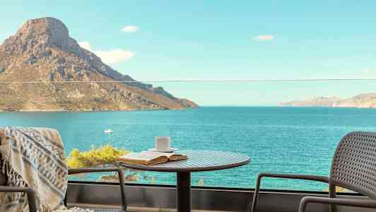 Et bord med en kopp og bok står på en balkong med utsikt over havet og et fjell. (AI-generert tekst)