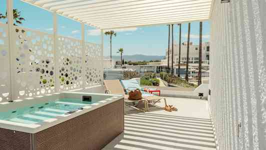 En terrasse med boblebad, solsenger og utsikt mot palmer og bygninger i bakgrunnen. (AI-generert tekst)