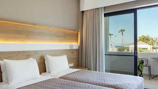 Hotellrom med to enkeltsenger og utsikt mot en uteplass og hav i bakgrunnen. (AI-generert tekst)