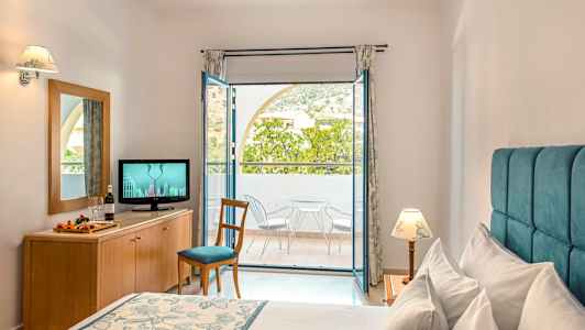 Et hotellrom med en seng, en kommode med en TV og en balkong med stoler og bord. (AI-generert tekst)