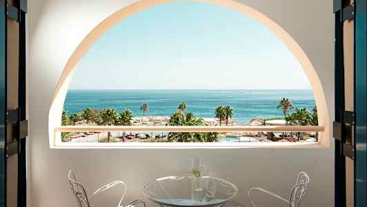 Utsikt fra en balkong med havet, palmer og et basseng i bakgrunnen. (AI-generert tekst)