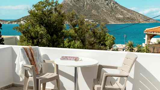 Utsikt fra en terrasse med to stoler og et bord, mot havet og en klippe i bakgrunnen. (AI-generert tekst)