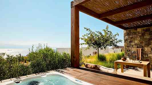 Bilde av en terrasse med et boblebad og hagemøbler, havet er synlig i bakgrunnen. (AI-generert tekst)