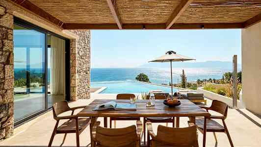 Utendørs terrasse med trebord og stoler, utsikt over basseng og hav. (AI-generert tekst)