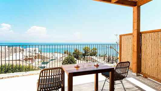 En terrasse med et trebord og stoler som vender mot en utsikt over havet. (AI-generert tekst)