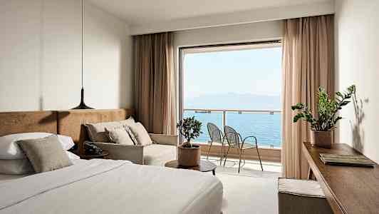 Et hotellrom med en seng, sofa og utsikt over havet fra en balkong. (AI-generert tekst)