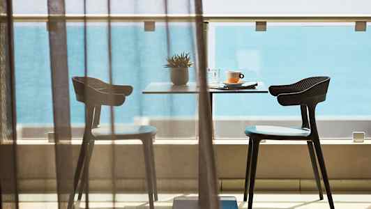 Et bord med to stoler på en balkong foran havutsikt. (AI-generert tekst)