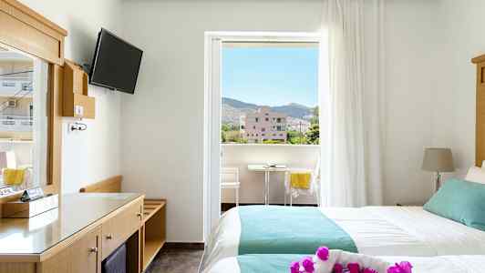 Hotellrom med to senger og balkong. Utsikt over omkringliggende bygninger og fjell. (AI-generert tekst)