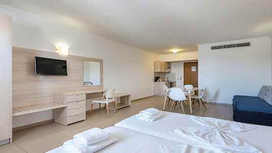 Et hotellrom med seng, skrivebord, TV og spiseplass med kjøkkenutstyr. (AI-generert tekst)