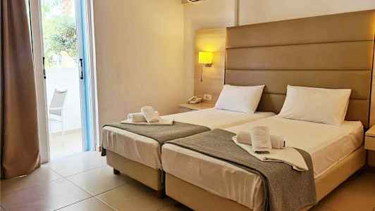 Hotellrom med to enkeltsenger, nattbord og en klimaanlegg på veggen. (AI-generert tekst)