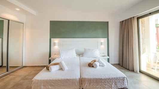 To enkeltsenger med hvitt sengetøy og sammenrullede håndklær, i et lyst rom med stor glassdør. (AI-generert tekst)