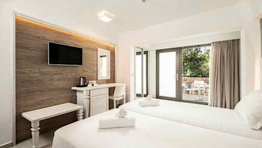 Et hotellrom med to senger, skrivebord, tv og en uteplass med bord og stoler synlig gjennom glassdører. (AI-generert tekst)