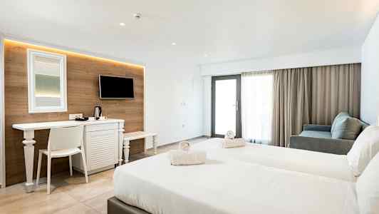 Et hotellrom med to senger, en skrivebord, TV og sittegruppe. (AI-generert tekst)