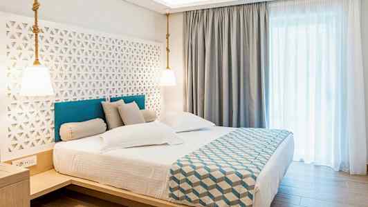 Hotellrom med en dobbeltseng, moderne innredning og lyse gardiner. (AI-generert tekst)