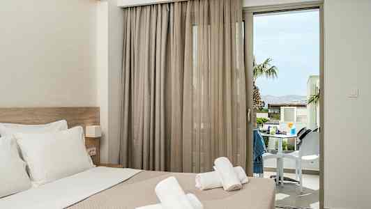 Hotellrom med oppredd seng og håndklær plassert oppå, med en balkongdør som vender mot en terrasse. (AI-generert tekst)