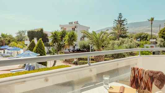 Balkong med bord, bok og glass; utsikt over hage og bygninger. (AI-generert tekst)