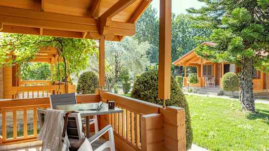 En treveranda med bord og stoler, omgitt av grøntområder og trehus. (AI-generert tekst)