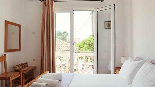 Et lyst soverom med hvite vegger, en seng med hvitt sengetøy og en balkong utenfor glassdører. (AI-generert tekst)