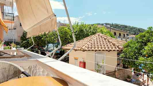 Utsikt over en solrik terrasse med tak og trær i bakgrunnen. (AI-generert tekst)