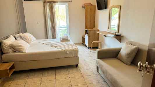 Et hotellrom med en seng, sofa, skrivebord og skap. Vinduet har lyse gardiner. (AI-generert tekst)