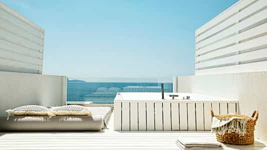 En hvit terrasse med et boblebad, puter og utsikt over havet. (AI-generert tekst)