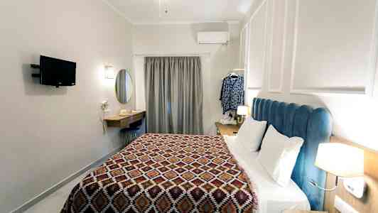 Et hotellrom med en seng, veggmontert TV, skrivebord og en gardin ved vinduet. (AI-generert tekst)