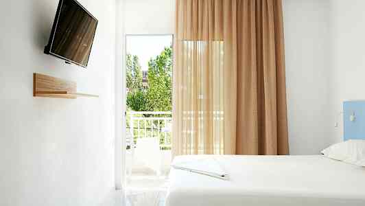 Et lyst rom med en seng, en veggmontert TV og en balkong med utsikt. (AI-generert tekst)