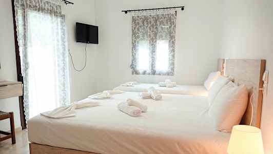 Et hotellrom med to senger, oppredd med hvite sengetøy og håndklær. En lampe på et nattbord og en veggmontert TV er synlige i rommet. (AI-generert tekst)