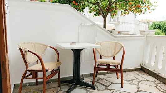 En liten uteplass med to stoler og et bord foran et appelsintre. (AI-generert tekst)