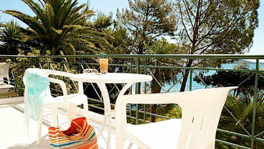 Utemøbler på en balkong med utsikt mot trær og vann. (AI-generert tekst)