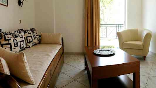 Et oppholdsrom med en sofa med geometriske mønstre, et rundt bord og en lys lenestol ved et vindu. (AI-generert tekst)