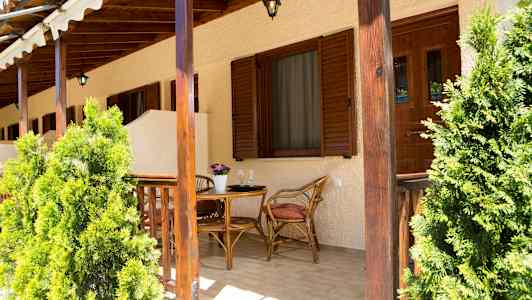 En uteplass med bord og stoler av tre, omgitt av grønne planter. (AI-generert tekst)