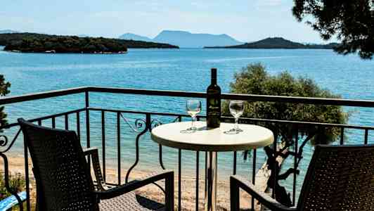 To stoler og et bord med en vinflaske og glass på en balkong med utsikt over havet. (AI-generert tekst)