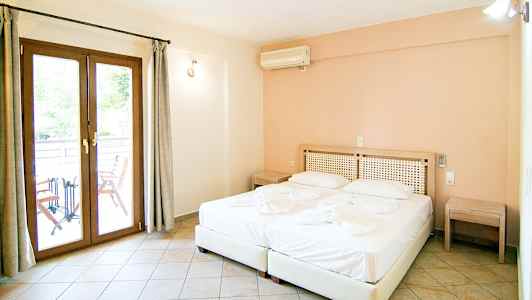 Et hotellrom med en dobbeltseng, to nattbord og en dør ut til en balkong. (AI-generert tekst)