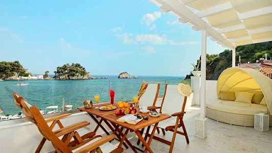 Utsikt fra en terrasse med spisebord og solseng mot havet og små øyer. (AI-generert tekst)