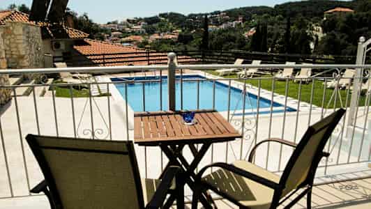 Utsikt fra en terrasse mot et basseng og et landskap med hus og grønne områder. (AI-generert tekst)