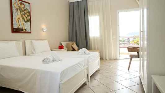 Et hotellrom med to enkeltsenger, hvite laken og håndklær. På veggen henger et maleri. Rommet har et vindu og en balkongdør. (AI-generert tekst)